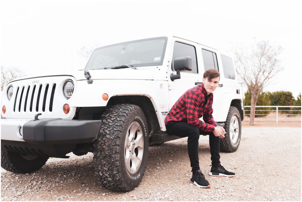 Senior guy wearing buffalo plaid shirt and posing next to jeep for portraits