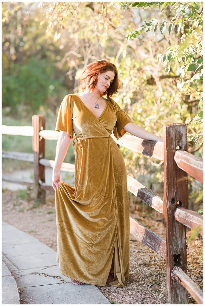 woman in gold velvet dress on autumn day by fence